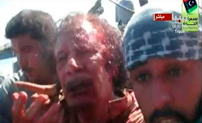 Former Libyan leader Muammar Gaddafi, covered in blood, is pulled from a truck by NTC fighters in Sirte in this still image taken from video footage