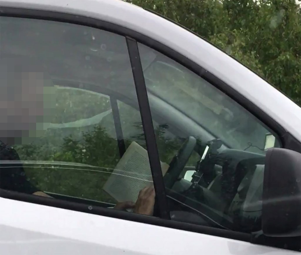  Footage shows the middle-aged motorist with a book propped up on the steering wheel during a rush-hour traffic jam on the M26 in Wrotham Heath, Kent.