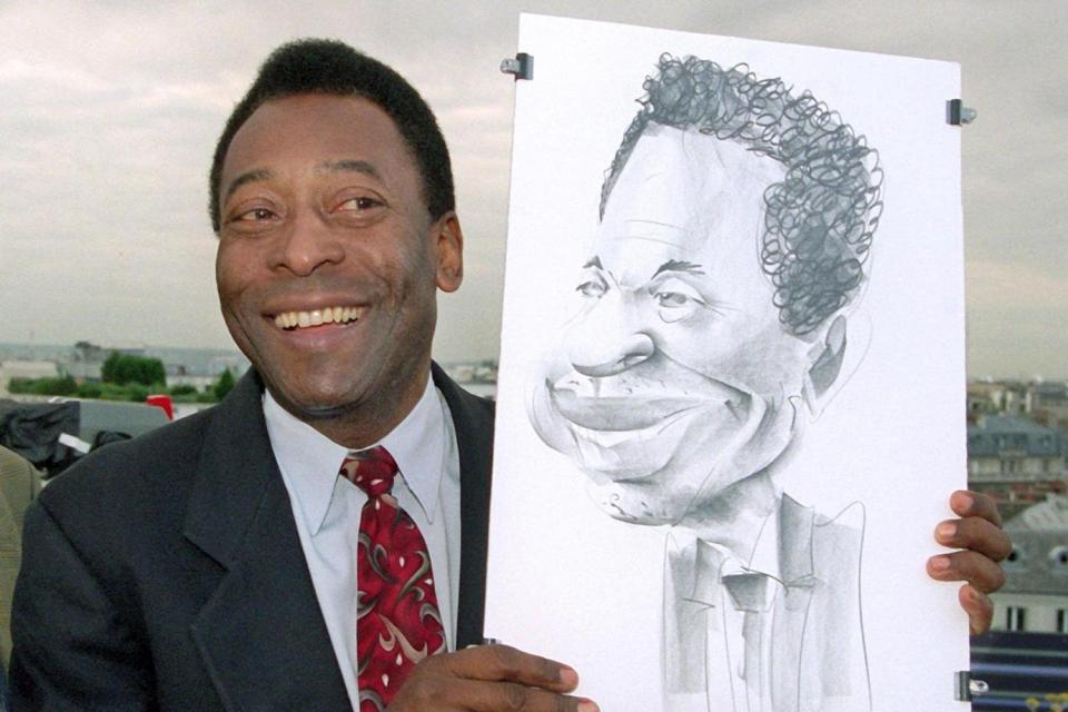  Pele poses with a caricature he was given which will now be sold