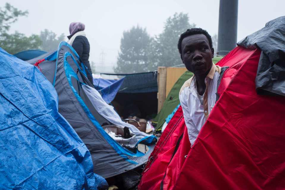  A migrant looks out of his tent as the scenes unfold. Many had been forced to use public standpipes to wash and drink from