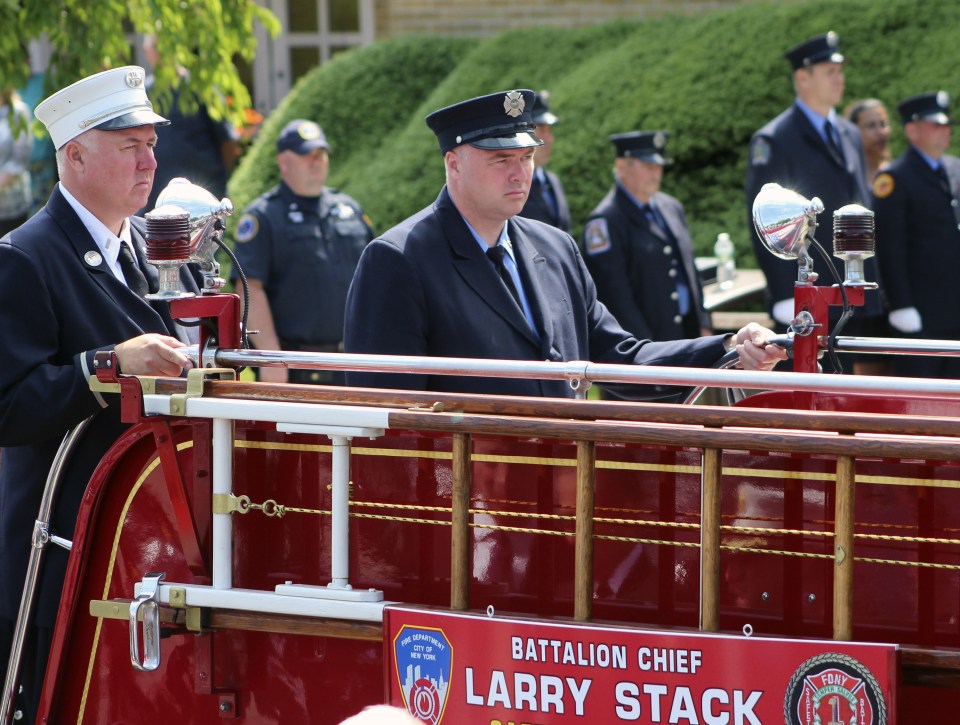 Michael Stack left, and firefighter Brian Stack, ride the back of a fire engine bearing the remains of their father