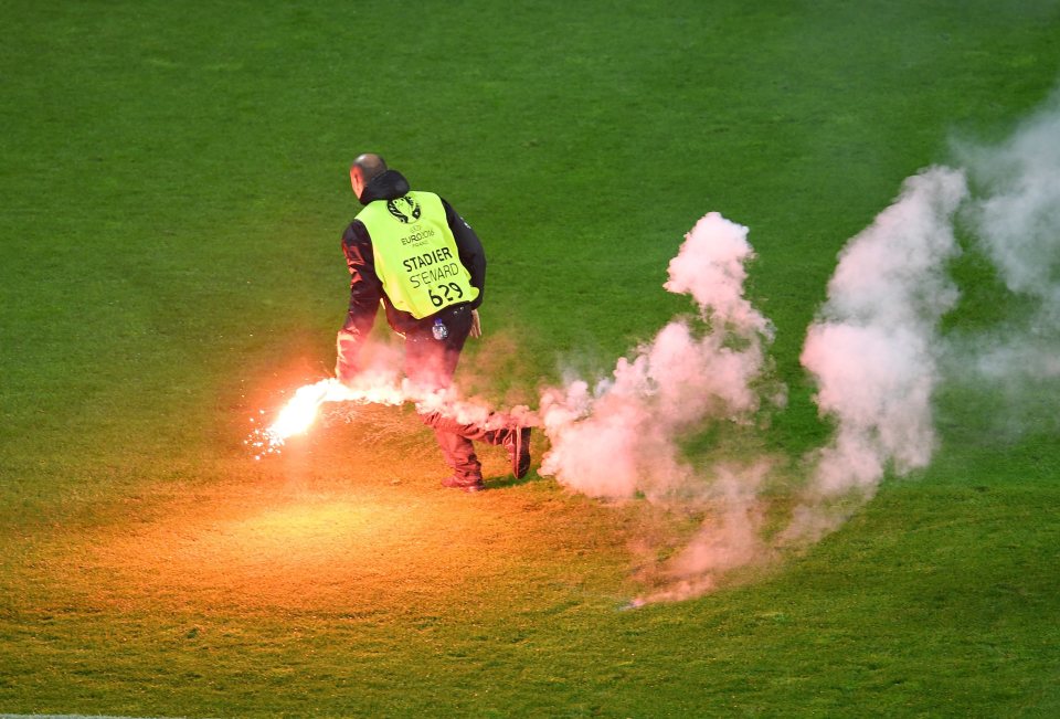  A steward removes a flare from the pitch during the game