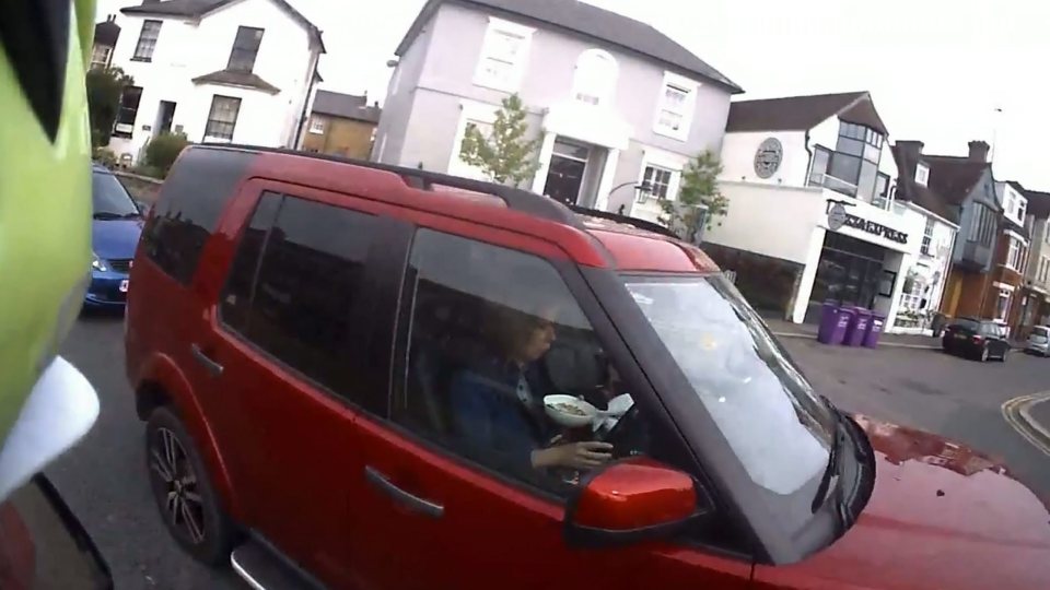 This is the moment a cyclist caught a middle-aged woman at the wheel of her Land Rover  eating a bowl of CEREAL. See swns story SWCEREAL. Raging cyclist David Williams, 47, had to perform a double take when he passed the red 4x4 on a busy commuter run after spotting her munching on her breakfast behind the wheel. He blasted her as bloody ridiculous after pulling over to find her with one hand on the steering wheel and the other clutching a bowl of what was believed to be Shreddies. Caught on the cycling instructors helmet camera, the footage shows the breakfast-eating woman as she sat in her £50,000 Land Rover Discovery in traffic in Hampton Court, Surrey, at around 8.45am on Tuesday. David, of Surbiton, south west London, banged on her window and warned: Put that down.Youre on camera. Youre going to the police. Ive got youre number. Absolutely ridiculous. Youre a bloody danger. The cereal offender drove off while still clutching her breakfast and David explained the situation to the driver who queued behind her.