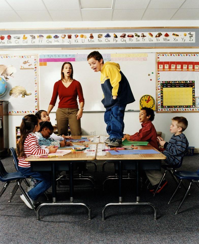 Boy (5-7) standing on desk in front of class