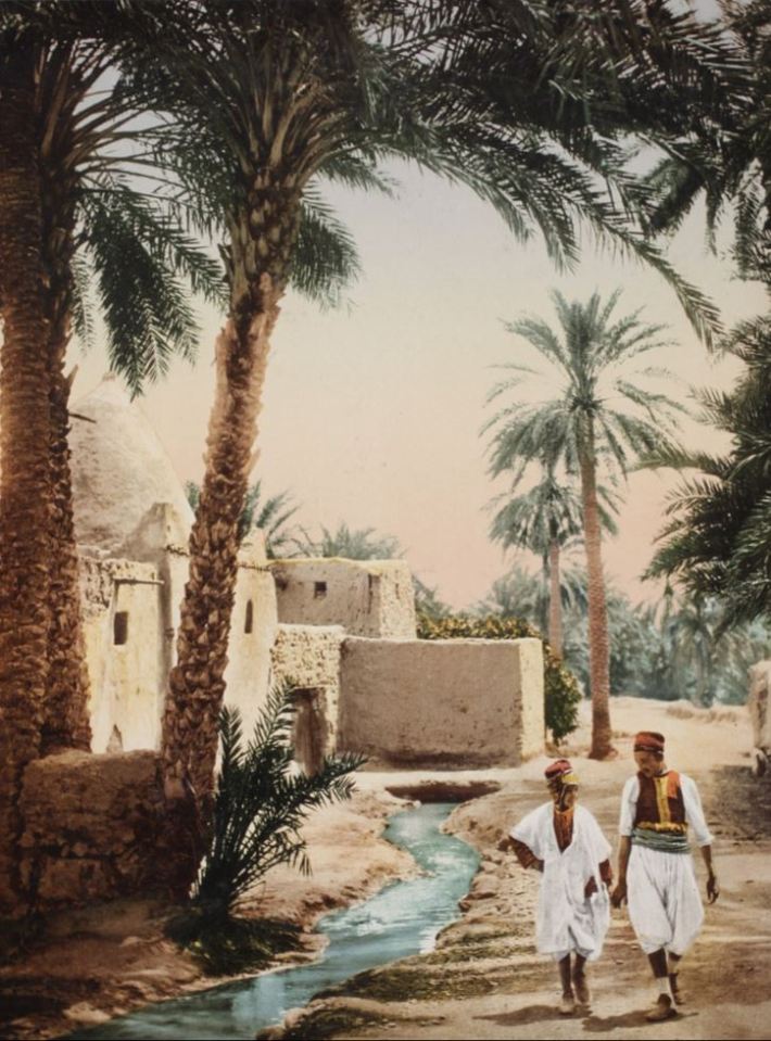 These scene shows a man and a child walking through Biskra, Algeria, in a scene captured over a century ago