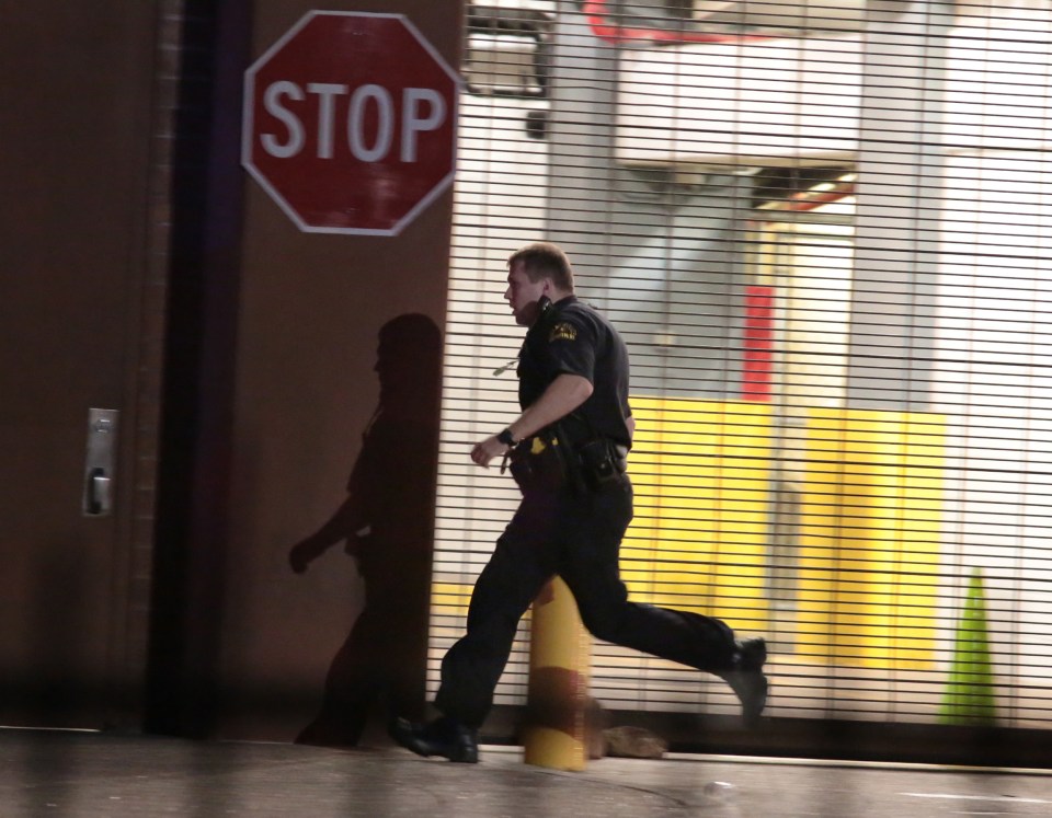  A Dallas police officer runs past a gated garage entrance where a sniper was threatening to set off bombs