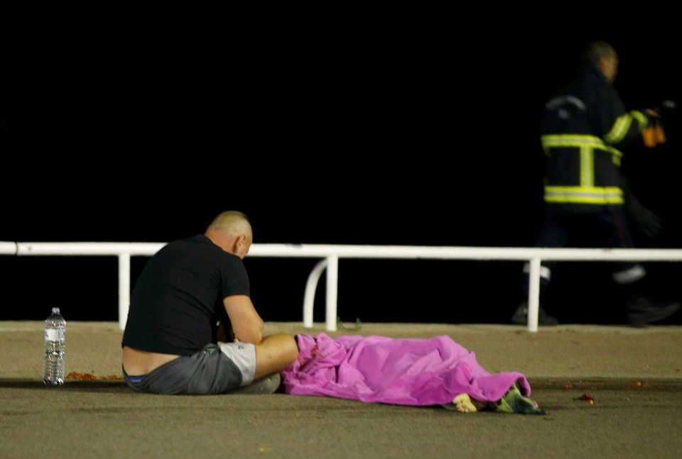  A man sits beside a covered-up body in the aftermath of the terror attack