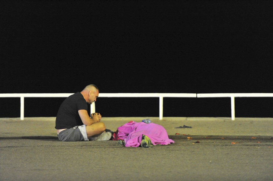  A man prays beside a body covered in a pink towel at the scene of the horror lorry attack in Nice