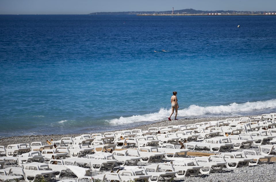  A lone woman walks along a deserted beach by the 'Promenade des Anglais'