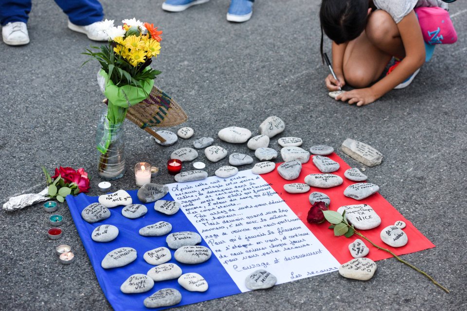  A woman writes a message on a stone to lay on a French flag with a memorial note, surrounded by flowers and candles, to pay tribute to the people who died