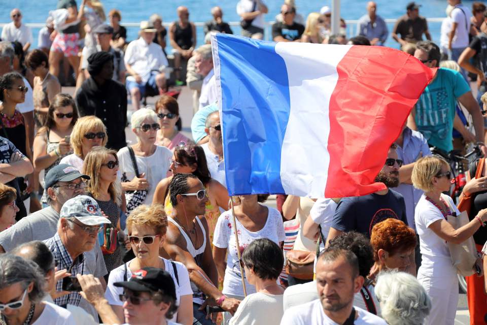  A man holds a French flag as people gather to observe a minute's silence on the Promenade des Anglais in Nice