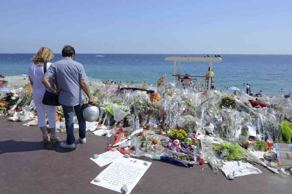 People stop near flowers left in tribute at a makeshift memorial to the victims in Nice