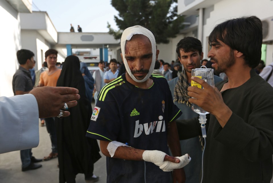  Afghans help a man who was injured in a deadly explosion in Kabul