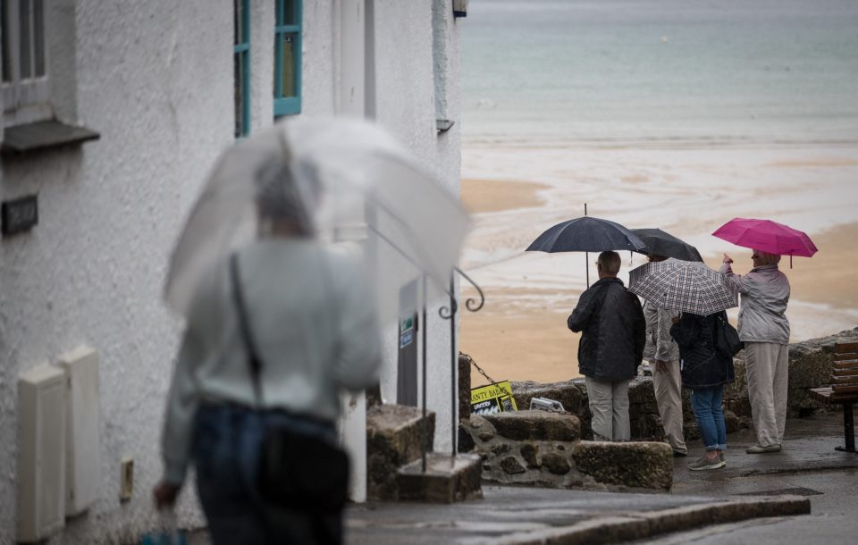  People stand under umbrellas as they admire the view besides the harbour in St Ives on August 1