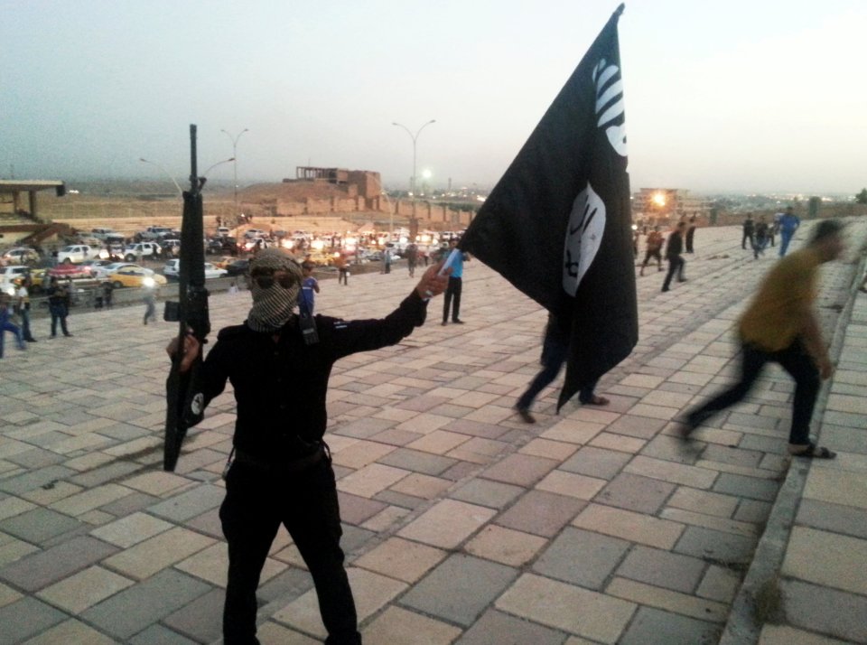  An ISIS fighter holds a terror flag and a weapon in Mosul on June 23, 2014