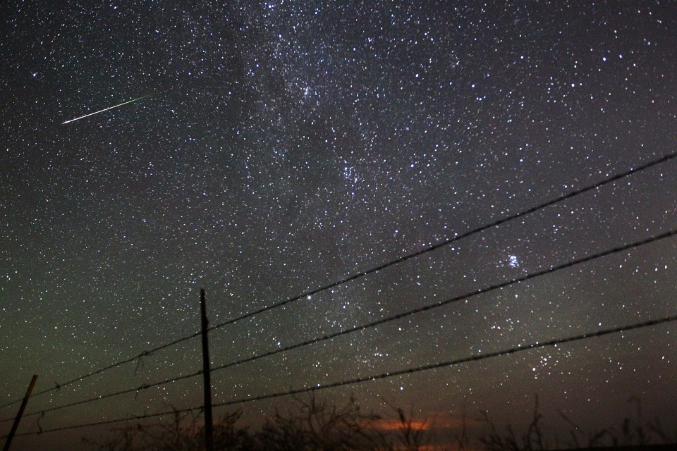  A meteor streaks past the faint band of the Milky Way galaxy above the Wyoming countryside in the USA