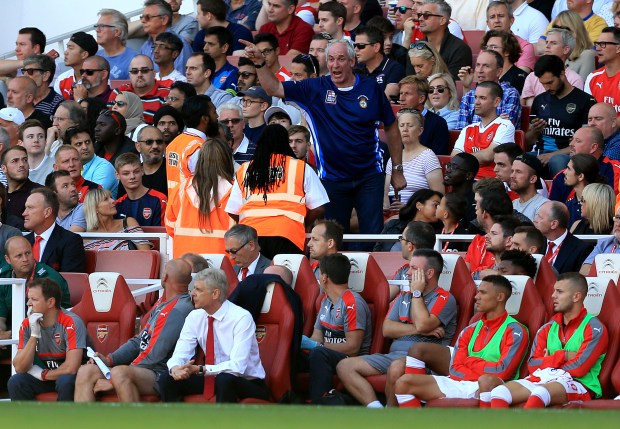 A fan in the stands exchanges words with stewards as Arsenal manager Arsene Wenger sits in the dugout