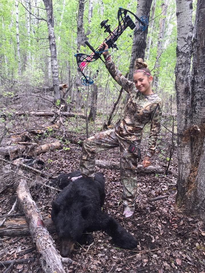  The schoolgirl is pictured standing on a slaughtered black bear while holding a hunting bow