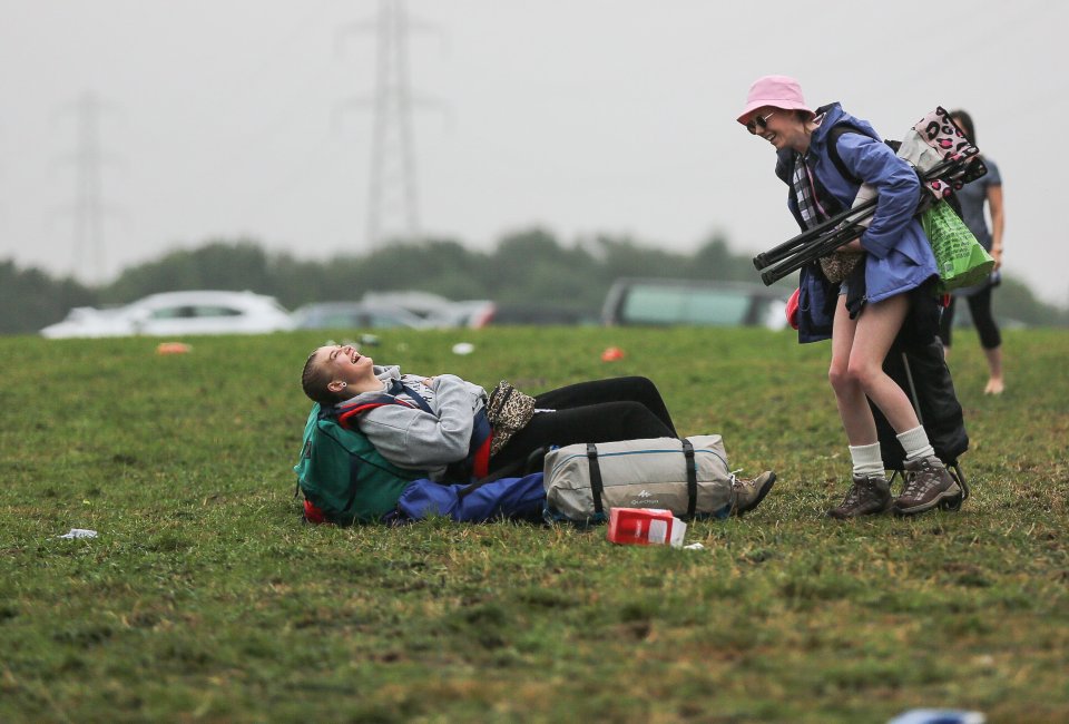  A women laughs as she falls to the floor with her backpack on as music lovers arrive at a damp Leeds Festival this morning