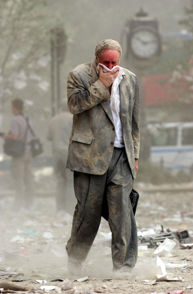 A man covers his mouth as he walks through debris