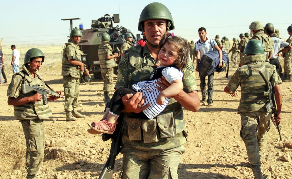 A Turkish soldier carries a Syrian girl as she crosses into Turkey