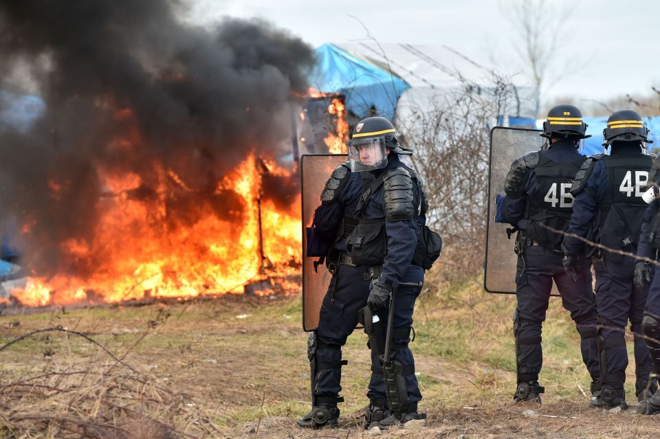  Anti-riot policemen stand near a shack burning in the "Jungle"migrant camp, Calais