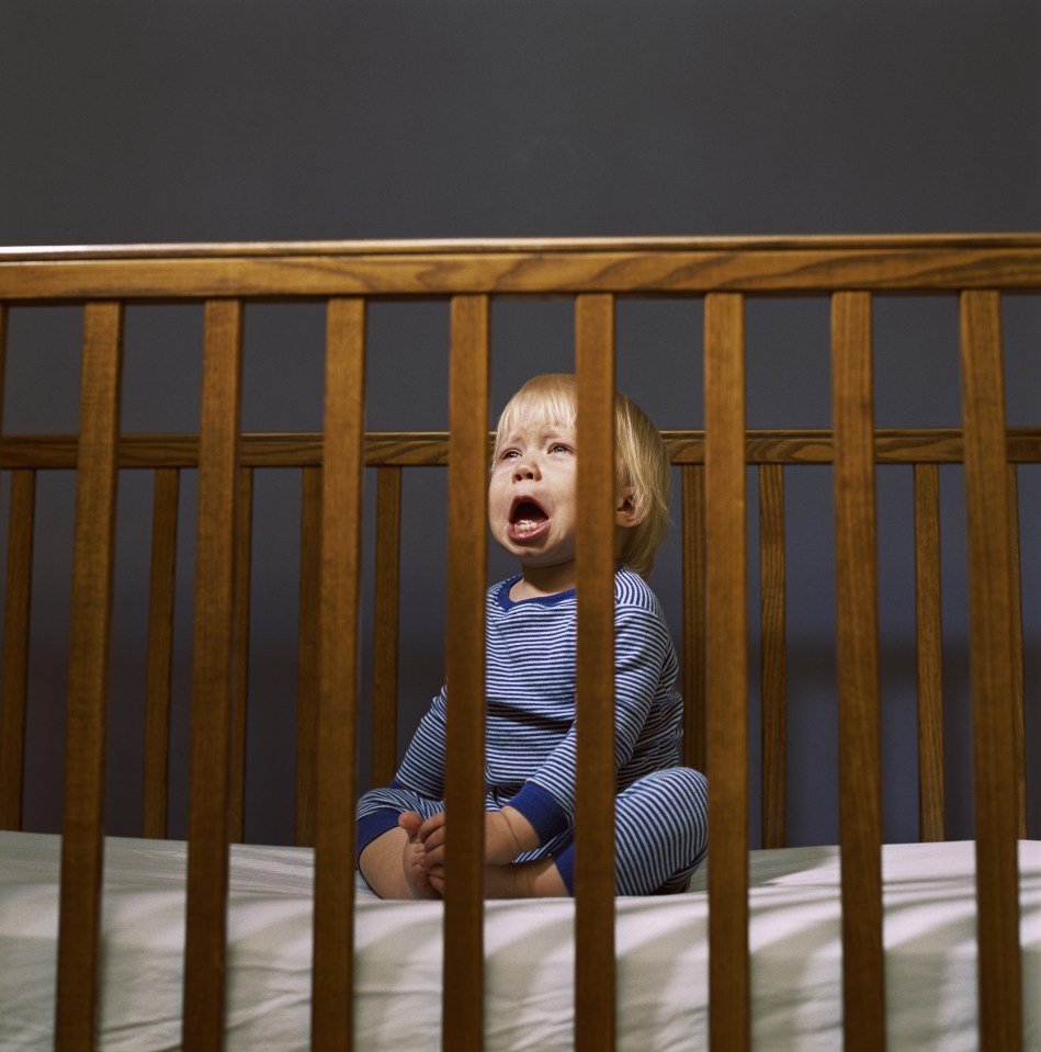 Crying toddler seated in crib