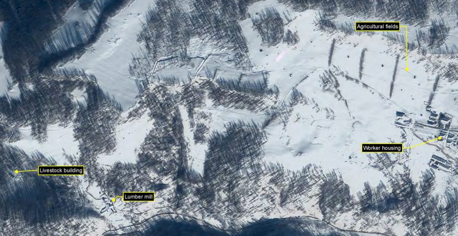 This snowy image shows livestock pens and a lumber mill are situated close to a housing centre