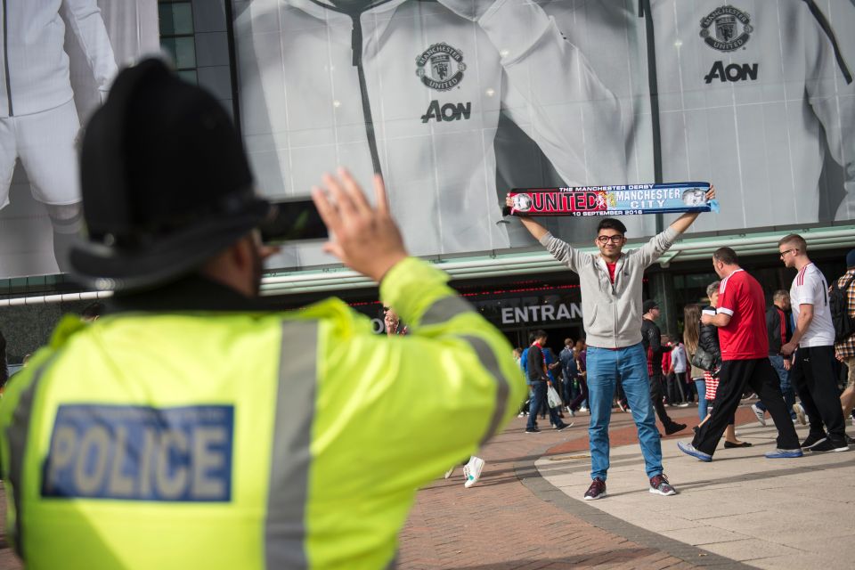  A police officer takes a photogrpah of a fan holding a scarf outside the ground