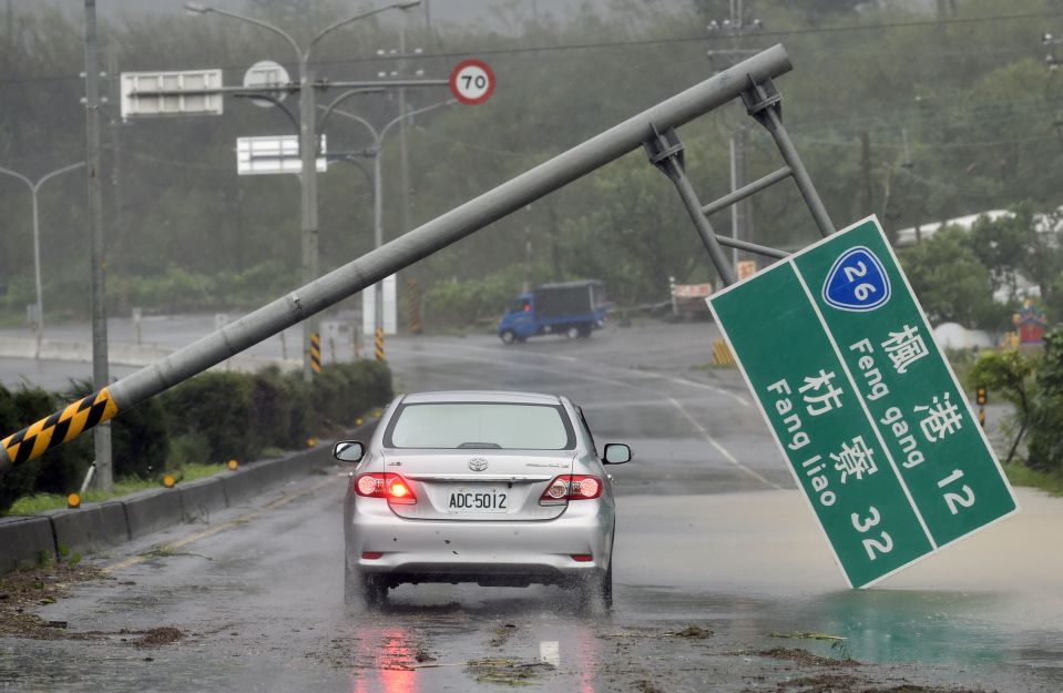  A car drives past a collapsed traffic sign which has been toppled by Typhoon Meranti