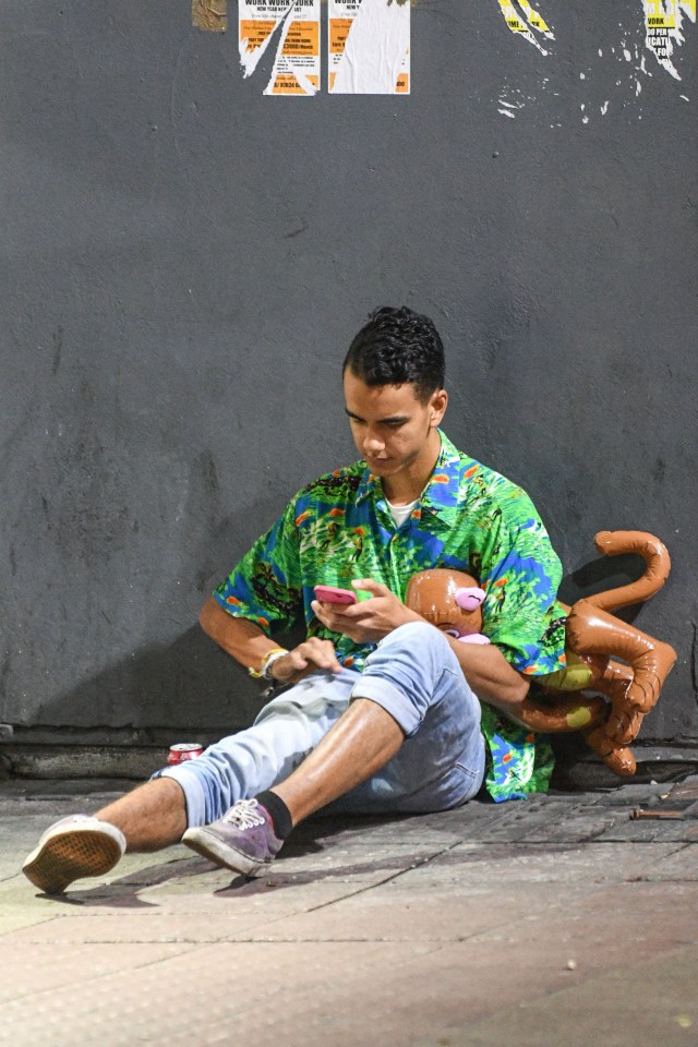  One reveller clutches a blow-up toy as he sits on the street to send a text