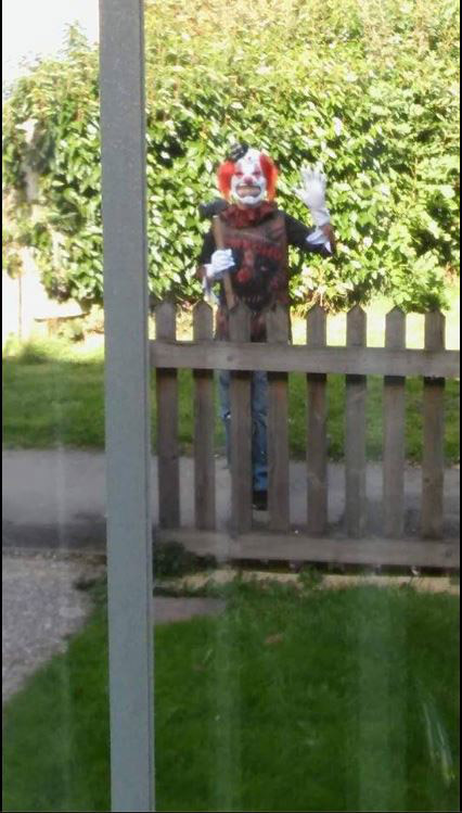  A clown in full fancy dress, holding a mallet or large hammer stood and waved at a passerby in Basingstoke