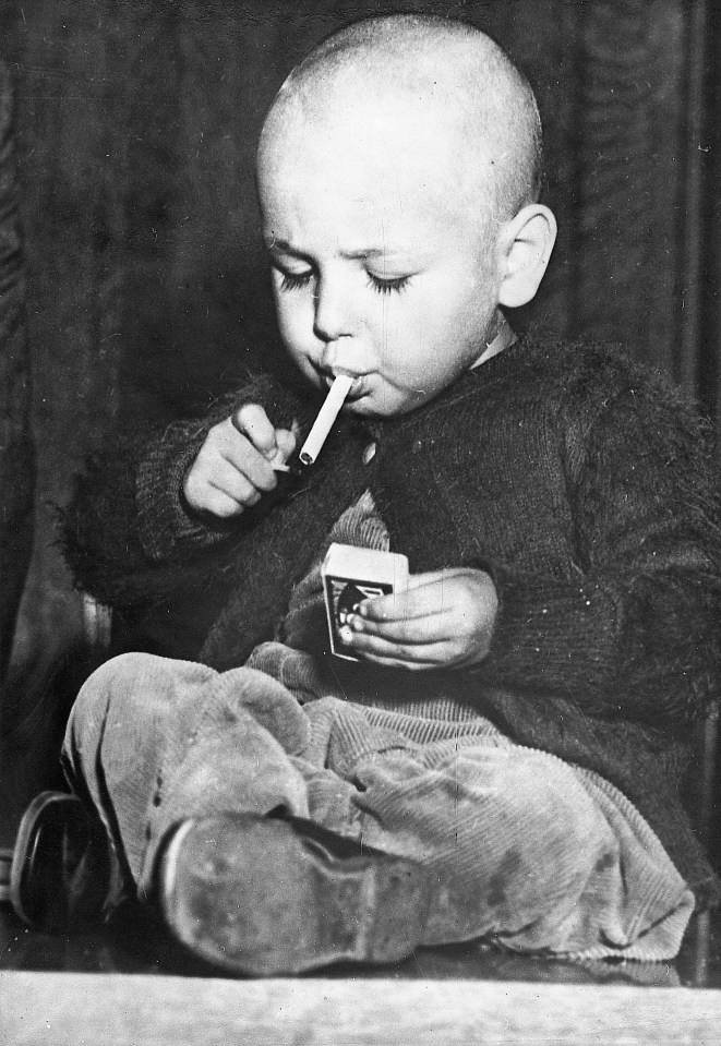 22-months-old boy lights a cigarette in a workmanlike manner. According to some information, he smokes from time to time a cigarette. Los Angeles. Photograph. Around 1920/30.