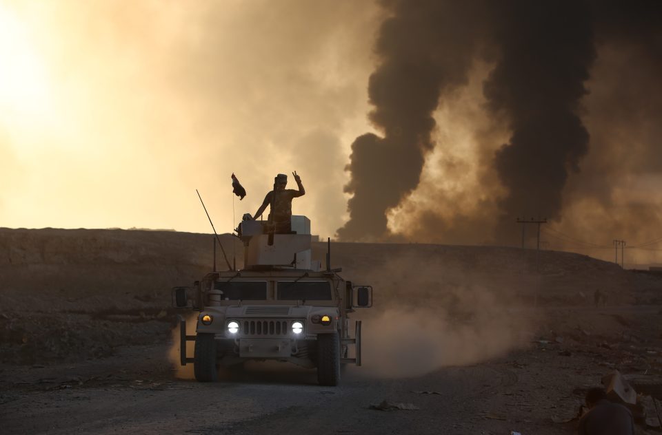  Iraqi army forces look out across a village where smoke rises from the burning oil wells