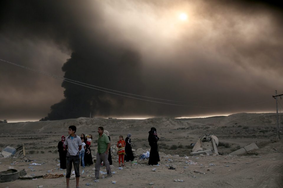  Smoke from burning oil wells rises behind a group of civilians forced from their homes by the fighting