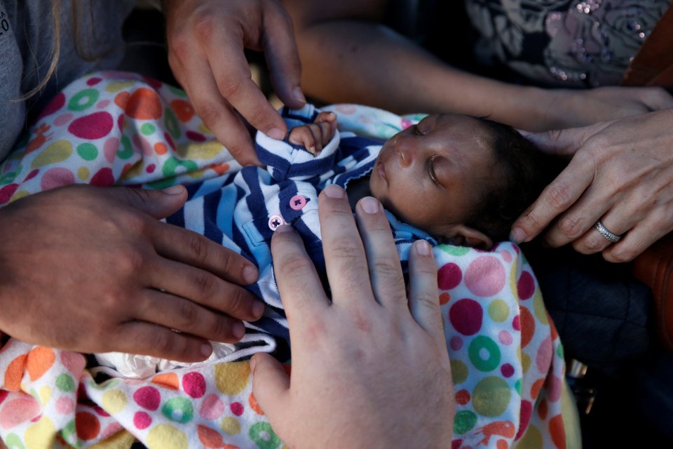 Aid workers stand over Micah and pray for him after he was abandoned by his parents