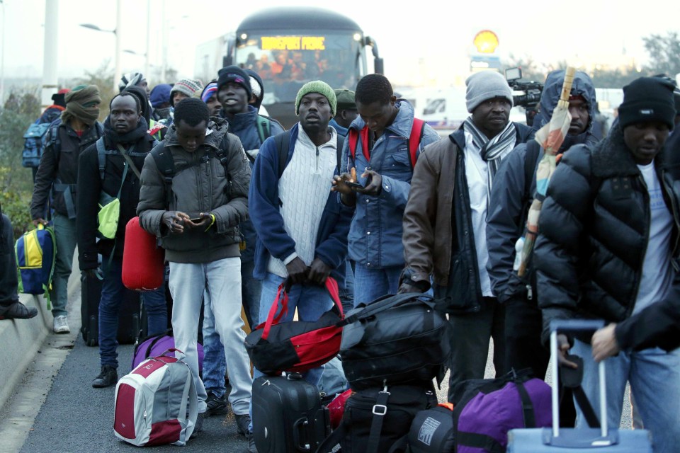 Migrants with their belongings queue near buses at the start of their evacuation