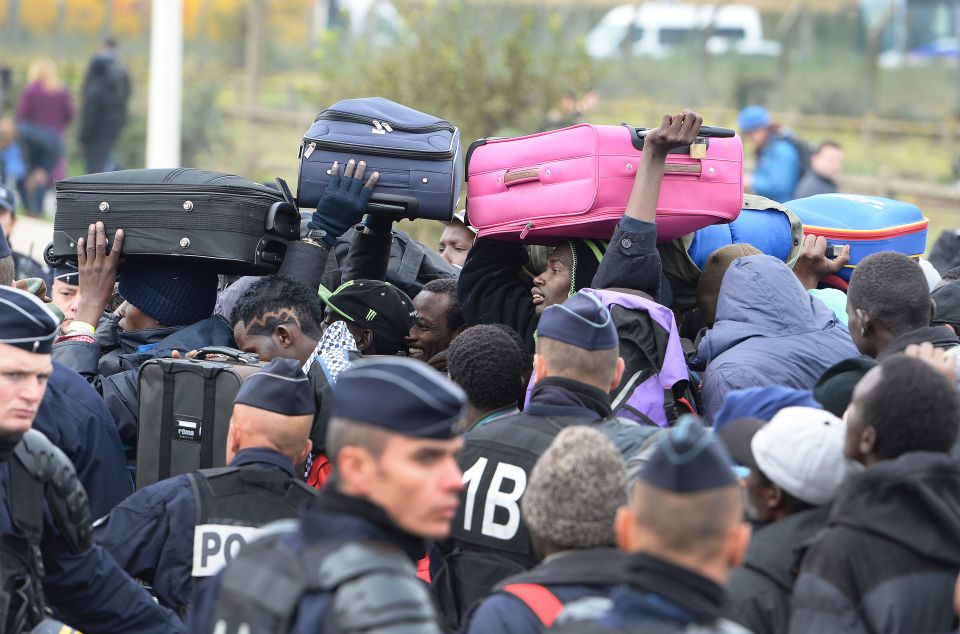  A group of men with suitcases jostle their way through a large queue of migrants