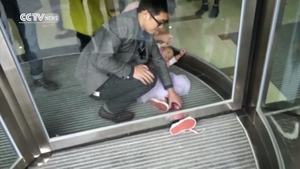  The little girl lies motionless on the ground while her leg is stuck in the revolving door