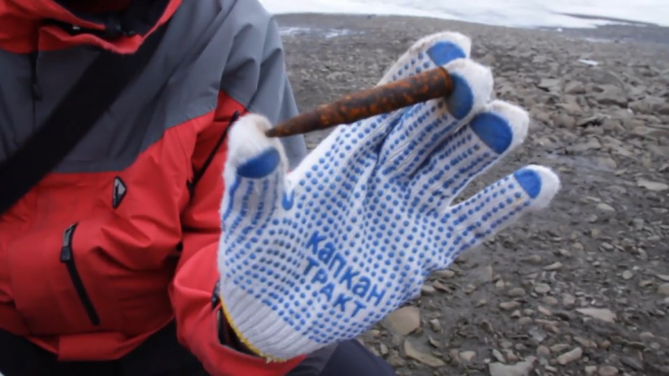  A scientist holds a rusted WWII bullet found on the frozen rocky ground