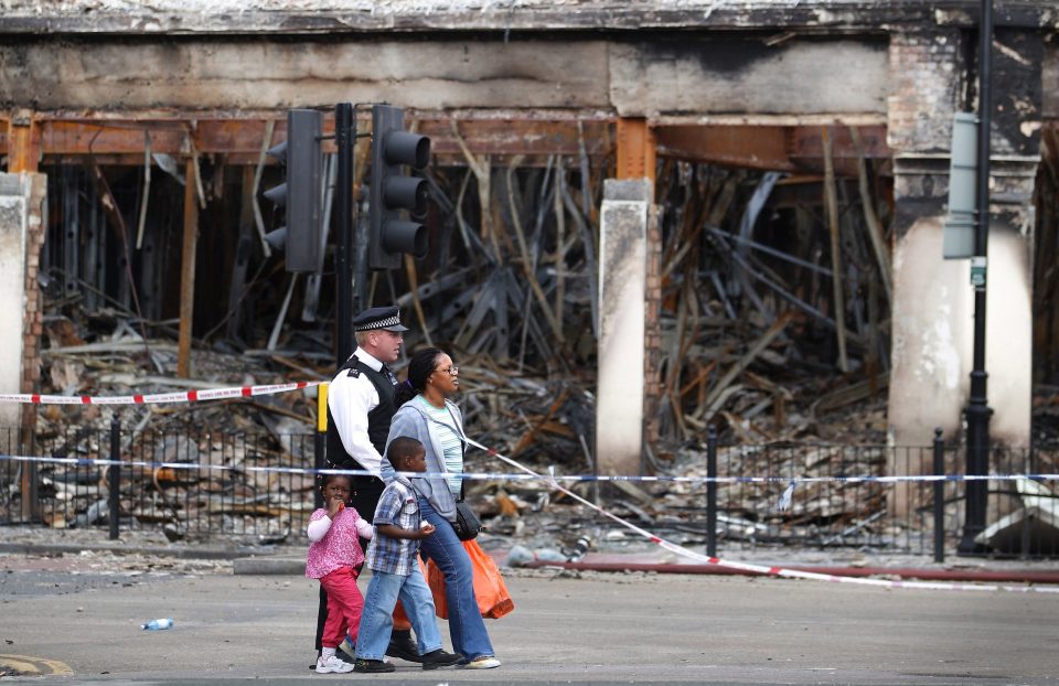  A police officer escorts a family past a burnt out Carpetright shop in Tottenham on August 8, 2011