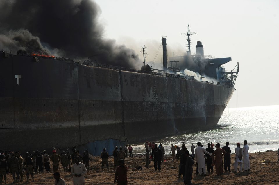 Bystanders gather around the wreckage of a burning ship after a gas cylinder explosion near Karachi, Pakistan