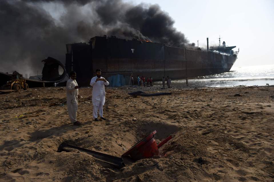 A Pakistani man takes pictures in front of a burning ship after a gas cylinder explosion at the Gadani shipbreaking yard