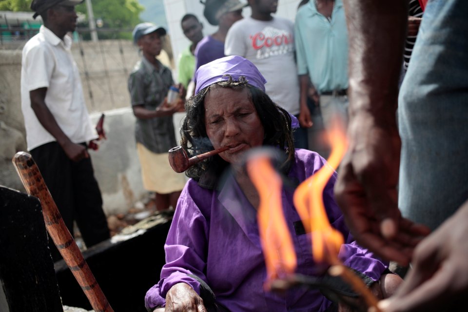  A voodoo believer dressed as "Gede smokes a pipe near one of the many fires in the cemetery