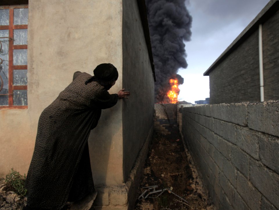  A woman looks at fire and smoke from oil wells on fire, with the flames leaving babies unable to breathe