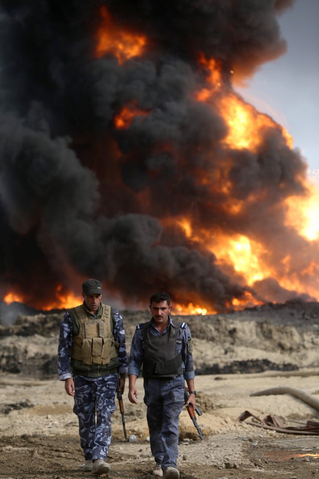  Iraqi security forces walk as fire and smoke rises from oil wells