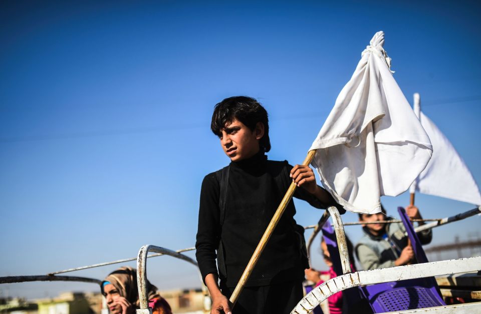  An Iraqi boy holding a white flag stands on a truck heading to camps for displaced people