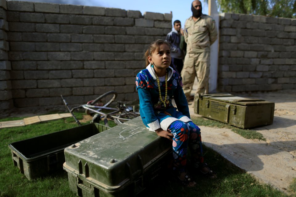  A girl sits on an empty ammunition box near an Iraqi soldier at her house's garden during a fighting with Islamic State fighters