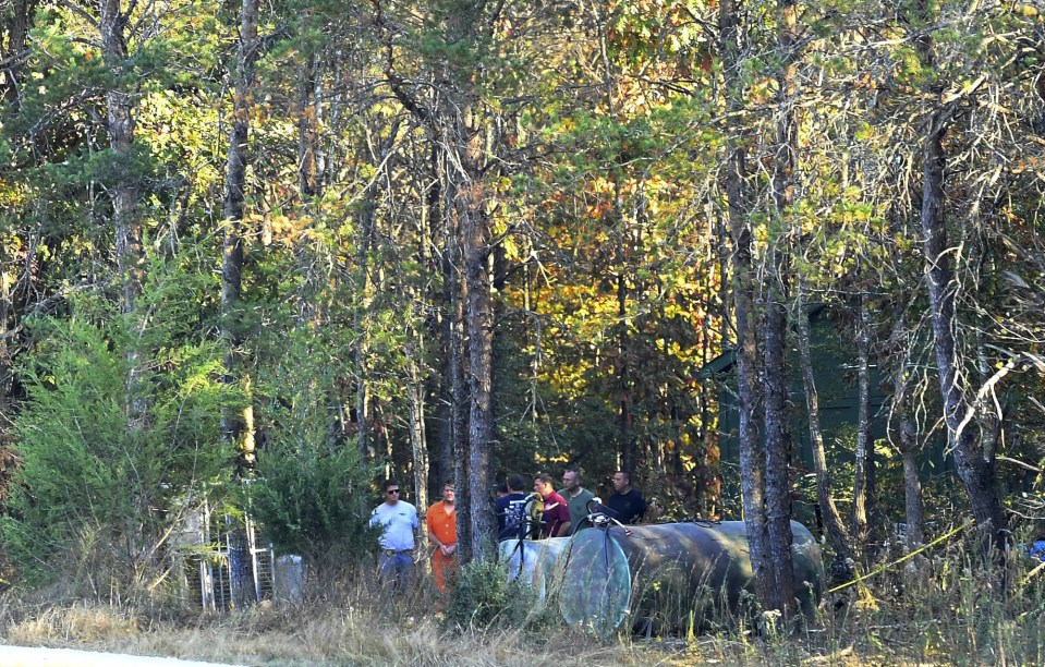  Todd Kohlhepp, in handcuffs and an orange jumpsuit, is escorted by deputies on his property, with a number of bodies found