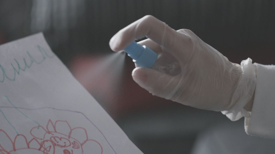 The woman is seen spraying a liquid form of a cannabis substitute onto children's drawings 